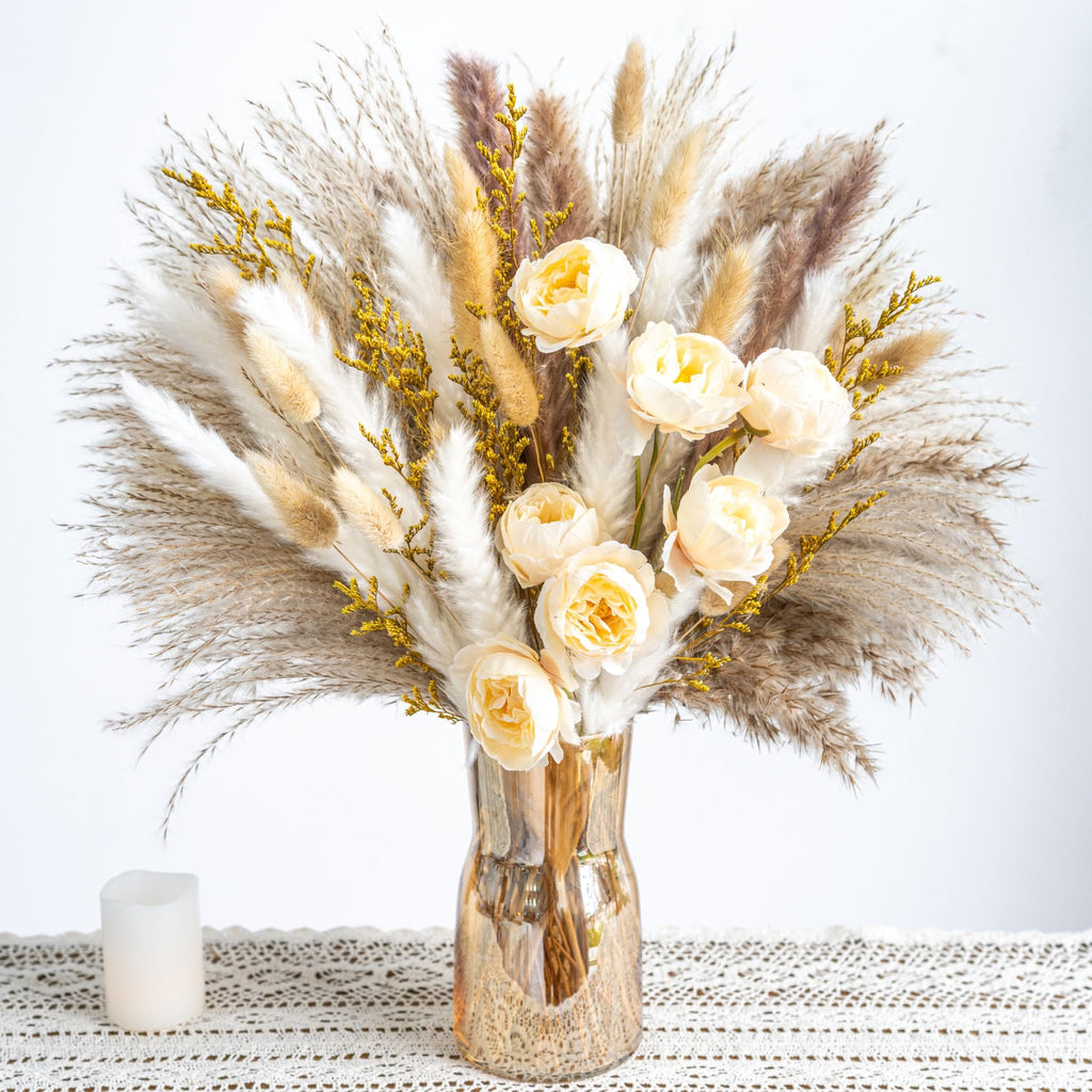 Boho pampas grass and dried flower bouquet in a gold vase with a white candle on a lace runner