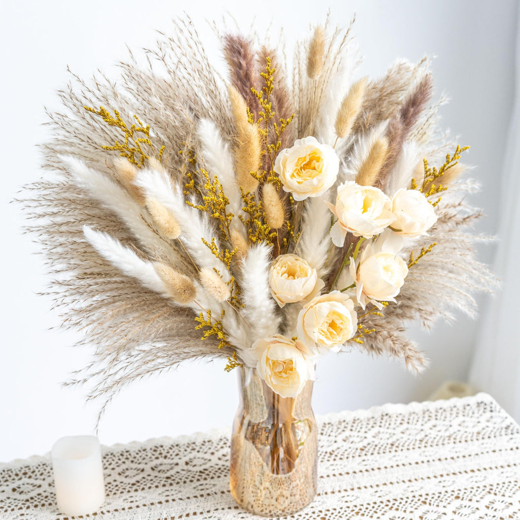 Boho dried flower and pampas grass bouquet in a textured amber vase on a lace tablecloth with a candle.