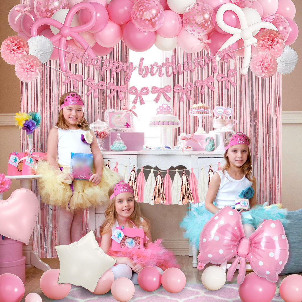 Pink birthday party decorations with girls in tutus, balloons, banner, and fringe curtain.