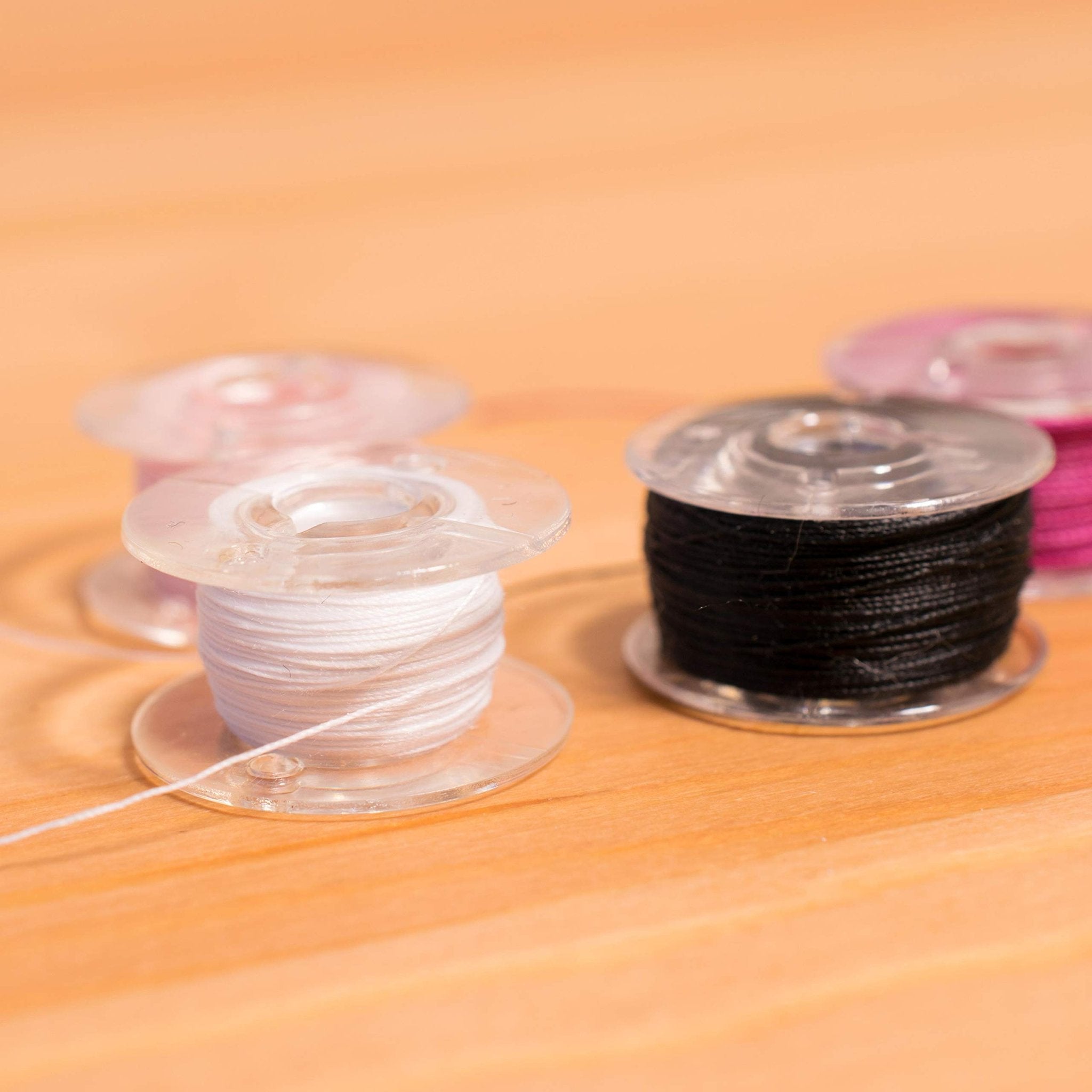 Close-up of sewing machine bobbins with white, black, and pink thread on a wooden surface.