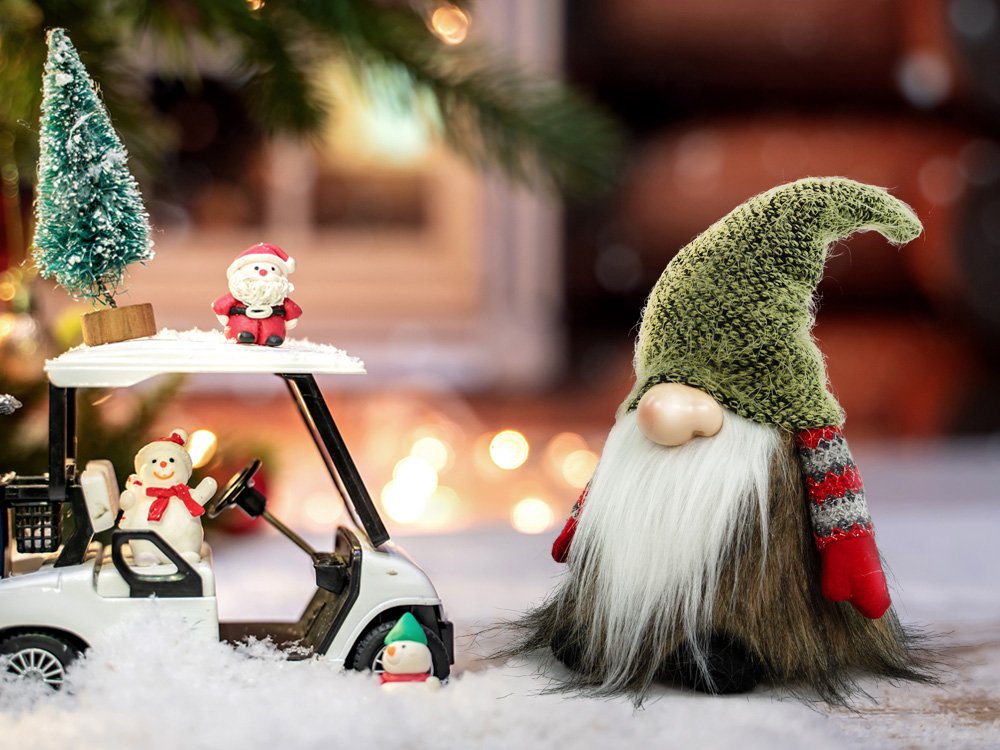 Christmas gnome decoration with a green knit hat and white beard, next to a miniature golf cart with Santa and snowman figures.