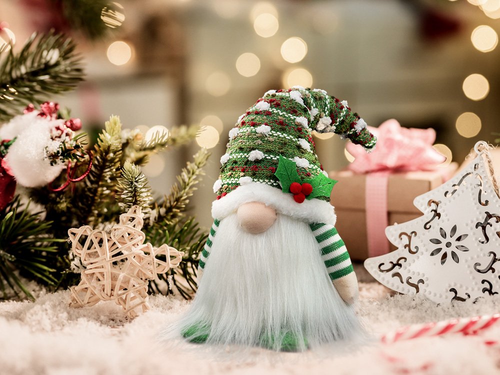Plush Christmas gnome with a green knit hat and white beard, surrounded by festive decorations.