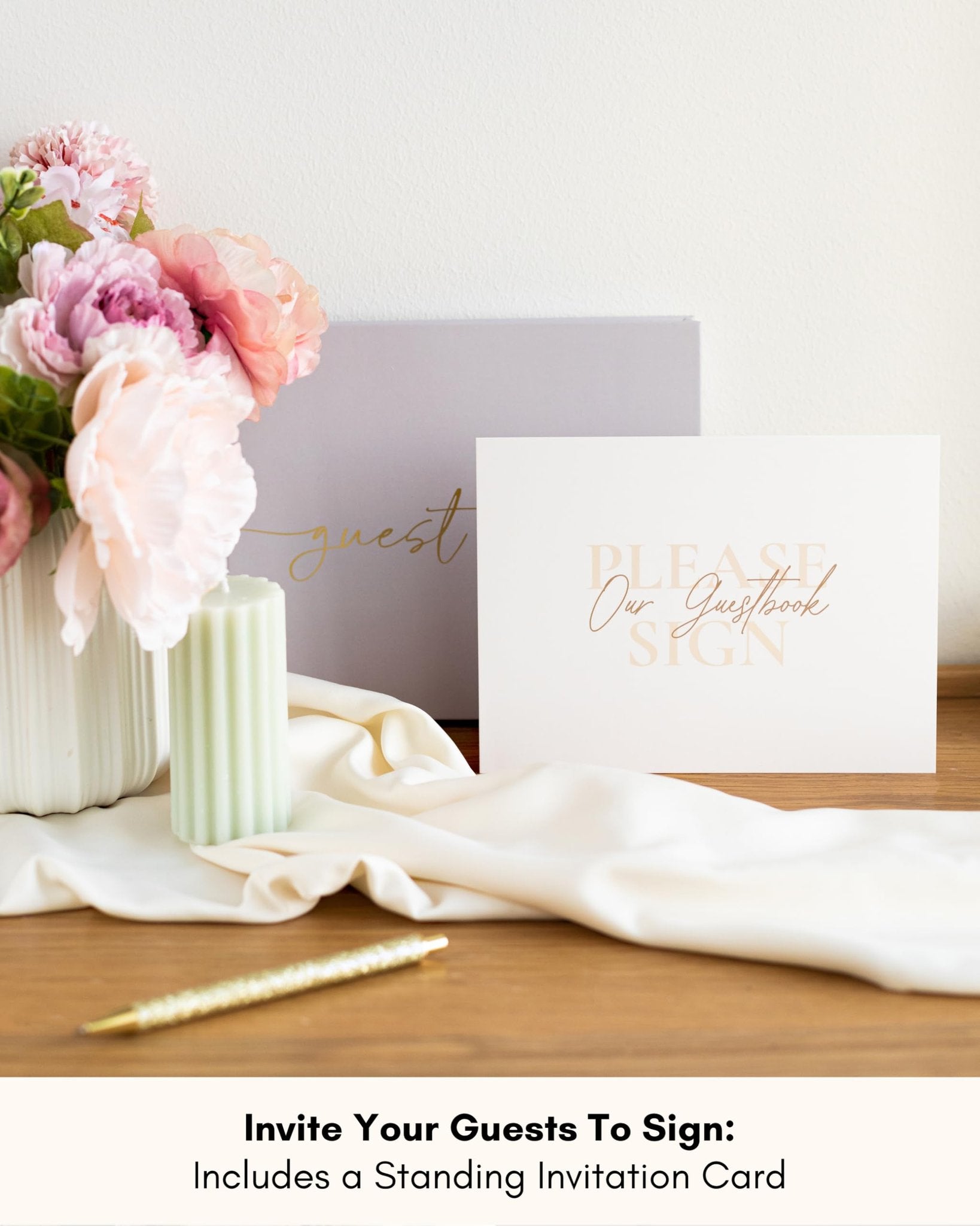 Wedding guest book setup with flowers, candle, pen, and invitation card that says 'Please Our Guestbook Sign'