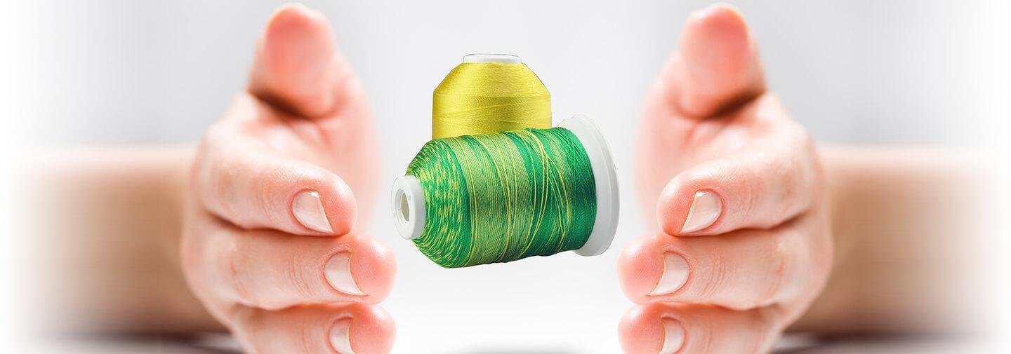 Two spools of embroidery thread, one yellow and one variegated green and yellow, held between two hands.