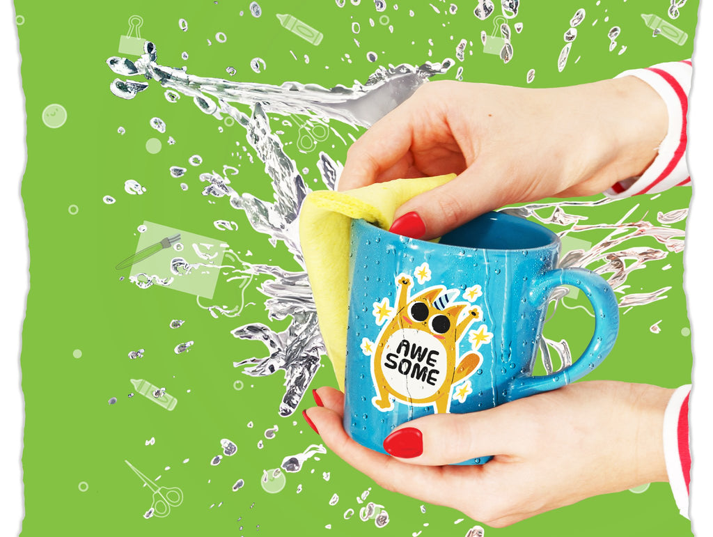 Hands cleaning a blue mug with a yellow sponge, showing a sticker of a cat with stars and the text 'AWE SOME'. Water splashes surround the mug.