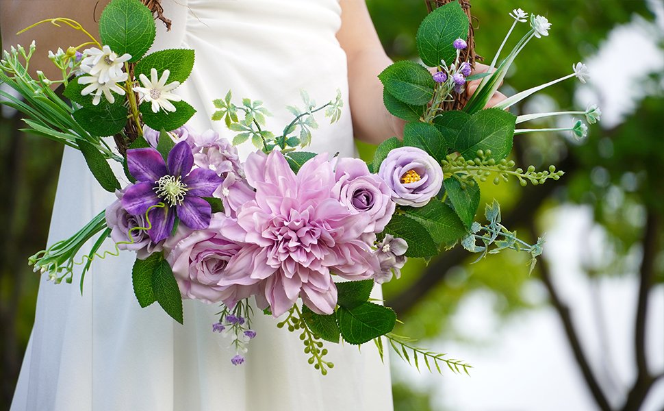 Person in white dress holding a purple artificial flower wreath with green leaves and various blooms