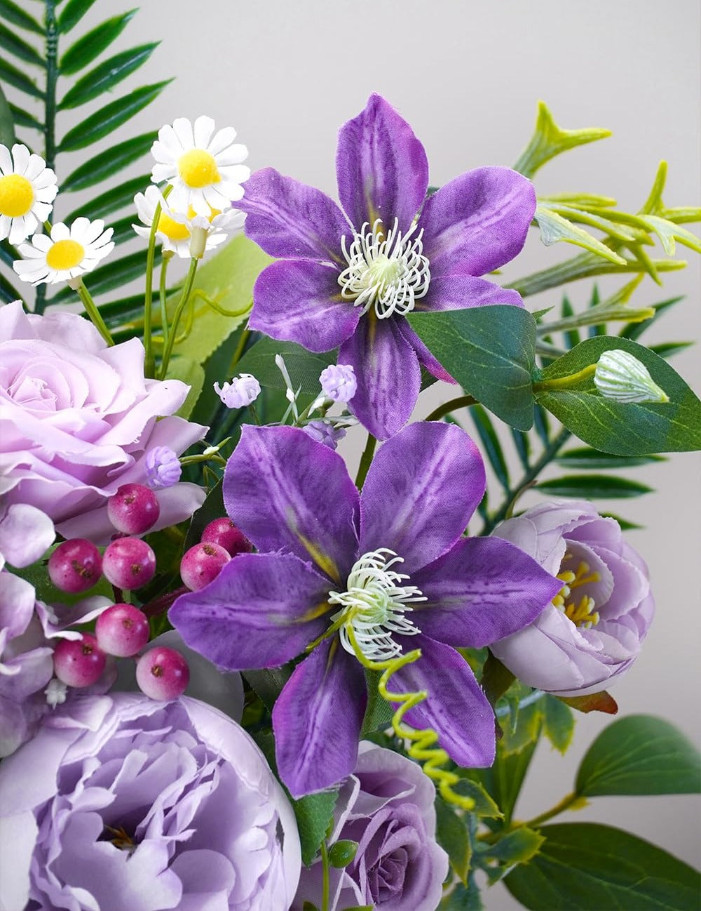 Close-up of a floral arrangement featuring purple clematis flowers, lavender roses, and small white daisies.