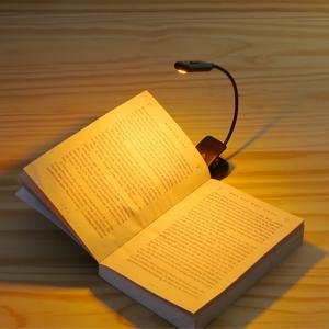 Black rechargeable clip-on book light illuminating an open book on a wooden surface.