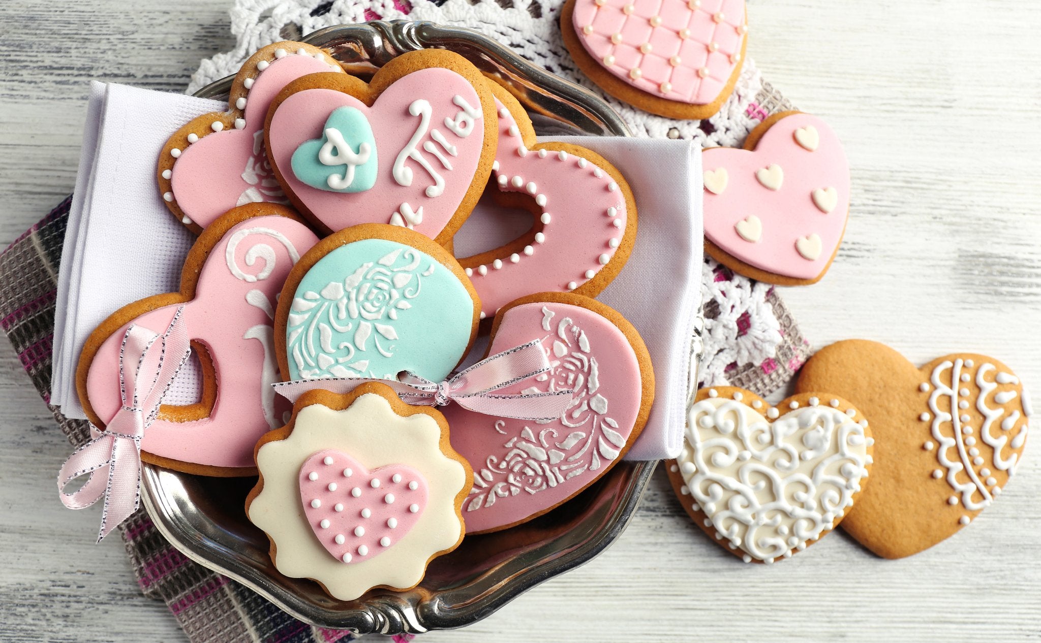 Assortment of heart-shaped cookies decorated with pink and teal icing and white royal icing designs, served on a silver platter with a white napkin.