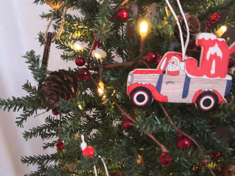 Close-up of a Christmas tree branch with a Santa in a red truck ornament and red berries.