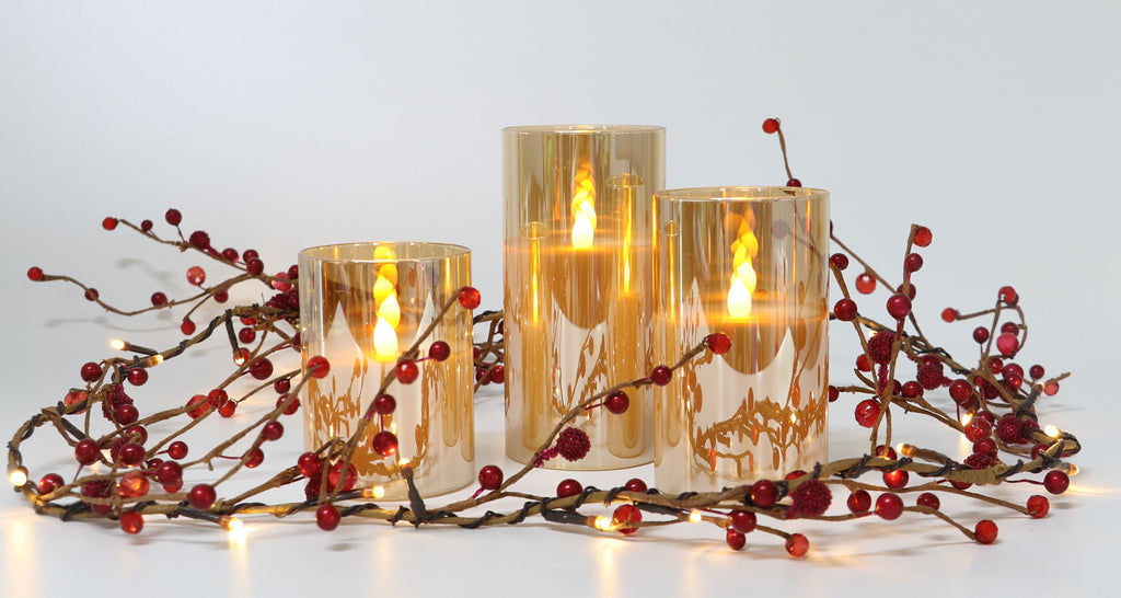 Three amber glass LED candles with flickering flames, surrounded by a red berry and LED light garland on a white background.