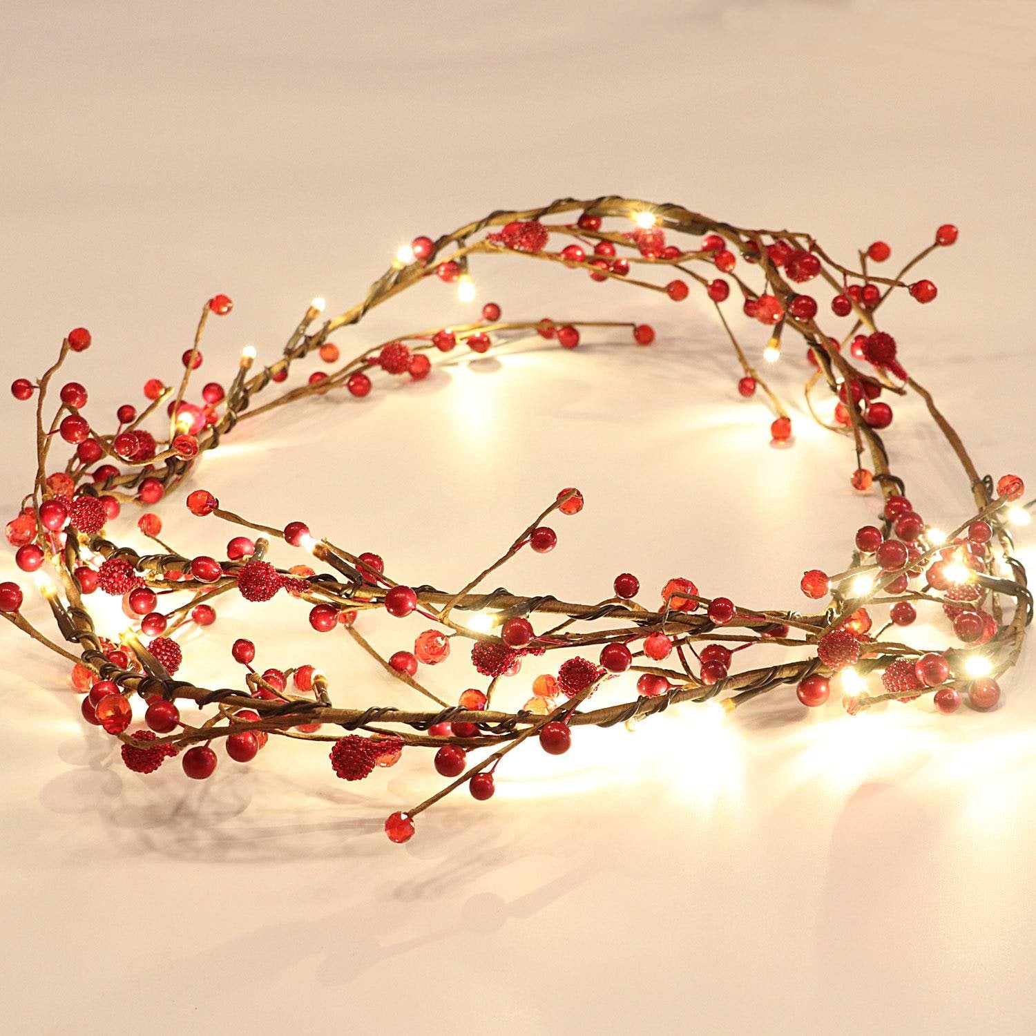 Red berry and LED light garland arranged in a curve on a white surface.