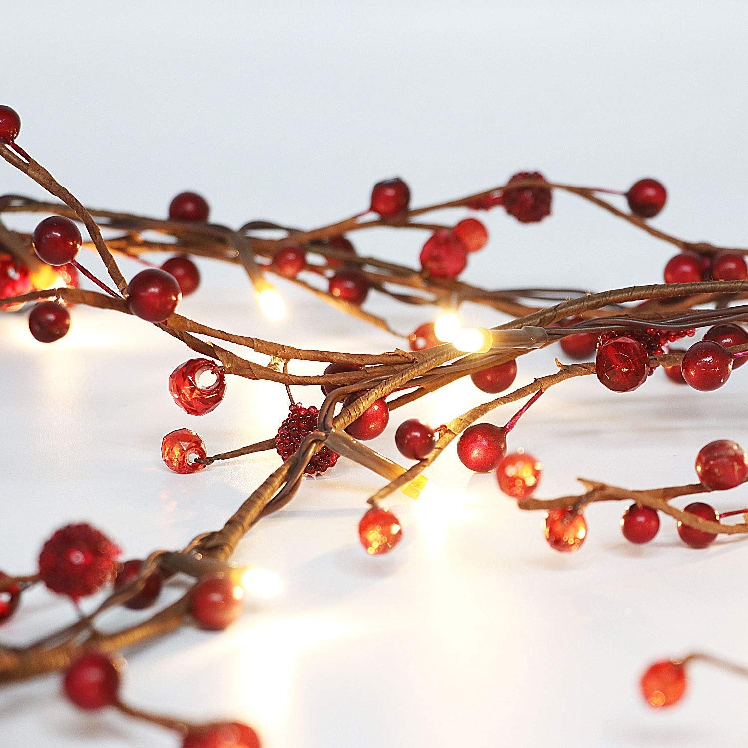 Close-up of a red berry and LED light garland on a white background, showing intricate details of the branches and berries.