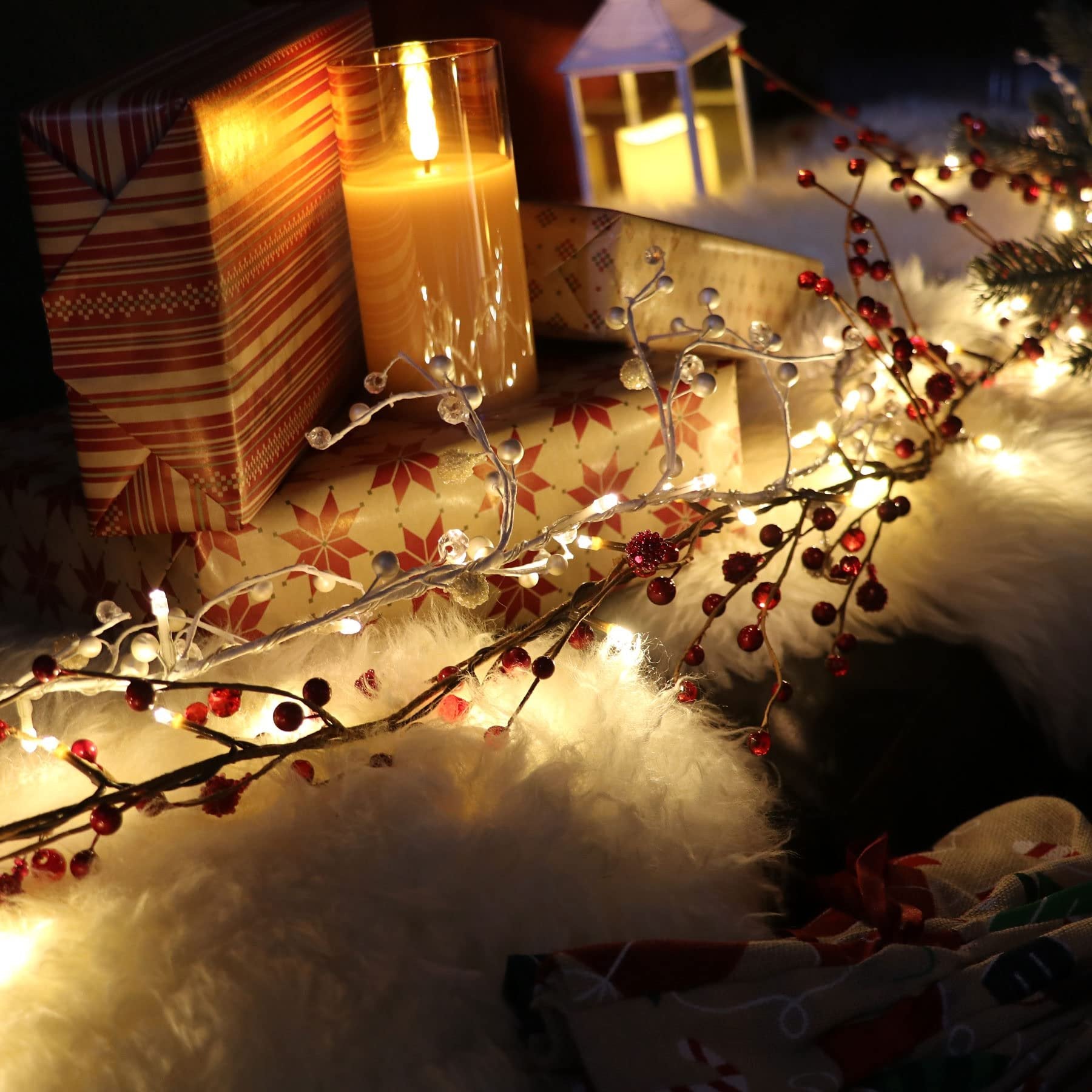 Red berry and LED light garland draped over faux fur with wrapped gifts and a candle.