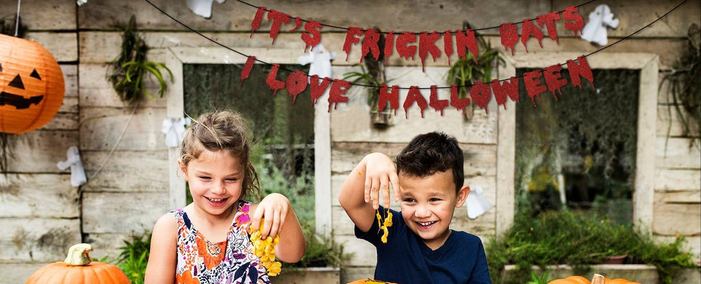 Children smiling with a Halloween banner that says "It's Frickin Bats I Love Halloween" hanging above them.