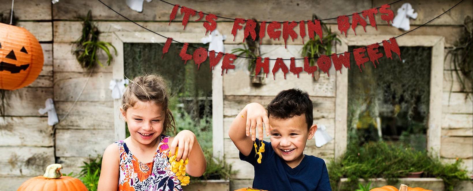 Children smiling with a Halloween banner that says "It's Frickin Bats I Love Halloween" hanging above them.