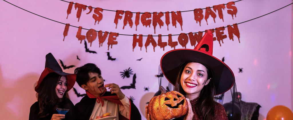 Halloween party with people in costumes and a glitter banner that says 'It's Frickin Bats I Love Halloween'