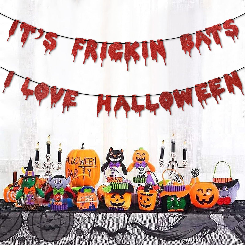 Red glitter Halloween banner with dripping letters reading 'IT'S FRICKIN BATS I LOVE HALLOWEEN' above a table of Halloween decorations.