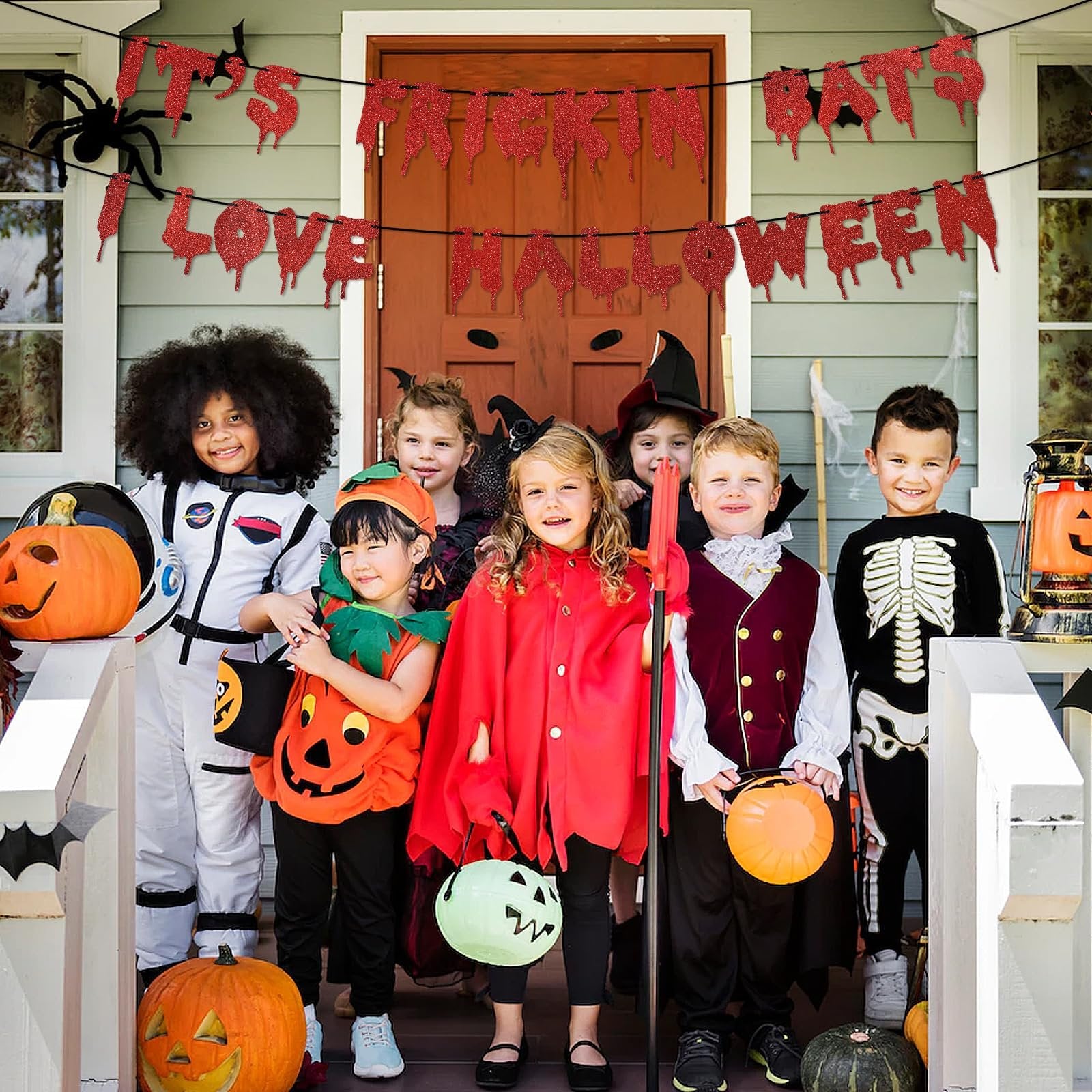 Children in Halloween costumes posing on a porch with a glitter banner reading 'It's Frickin Bats I Love Halloween'