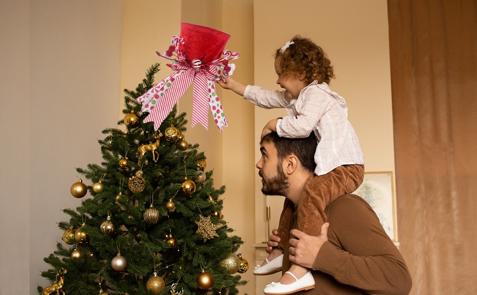 Father and daughter placing a red velvet candy cane Christmas tree topper on a decorated tree