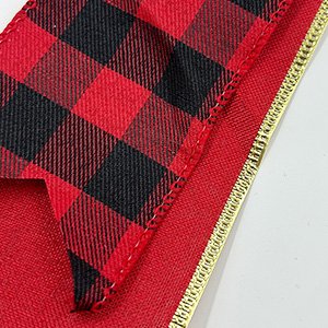 Close-up of a red and black buffalo plaid ribbon with a gold edge, part of a Christmas tree topper.