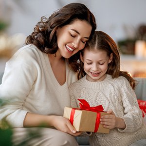 Mother and daughter opening a Christmas gift together, both smiling warmly.