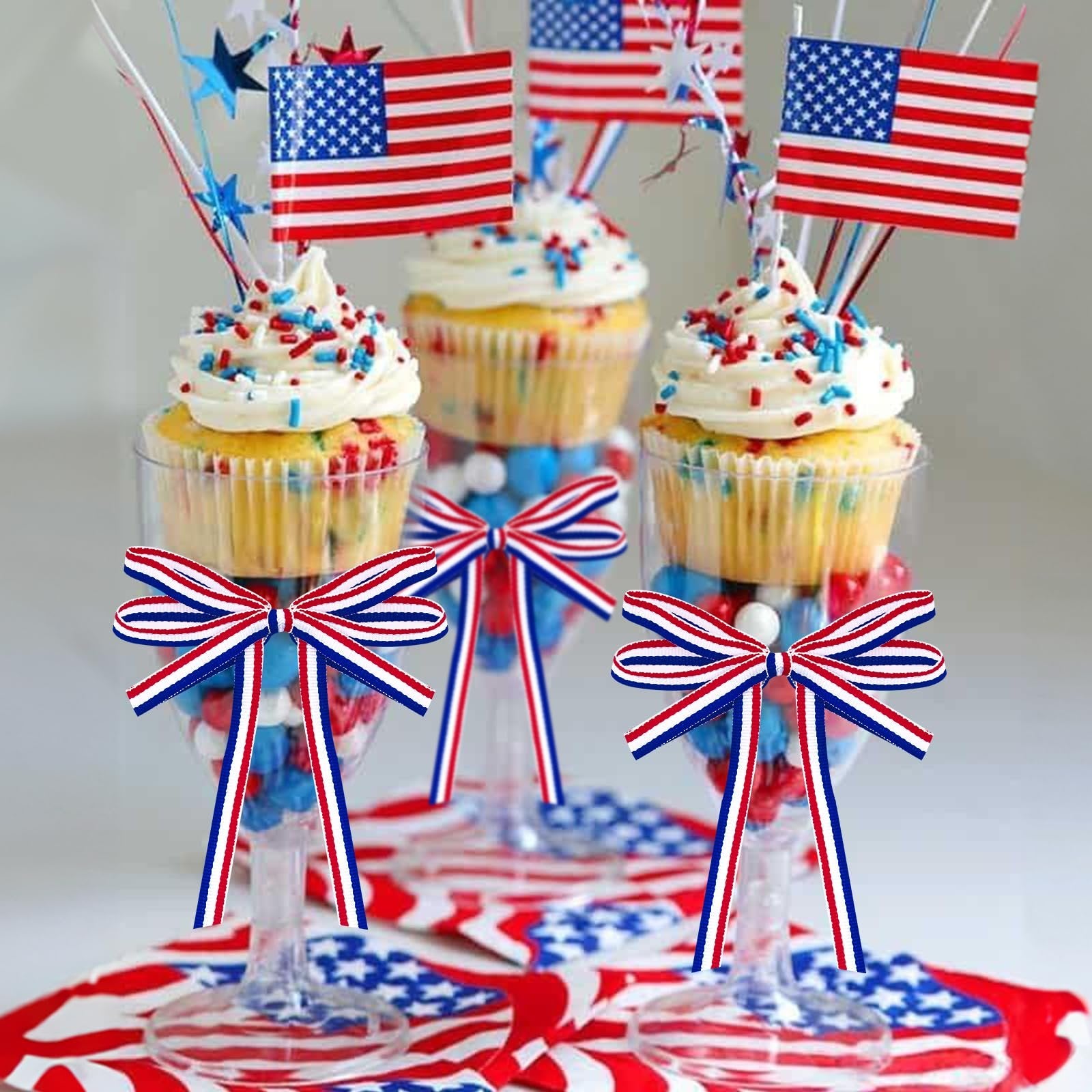 Patriotic cupcakes decorated with American flags and red, white, and blue sprinkles in clear glasses filled with candy.