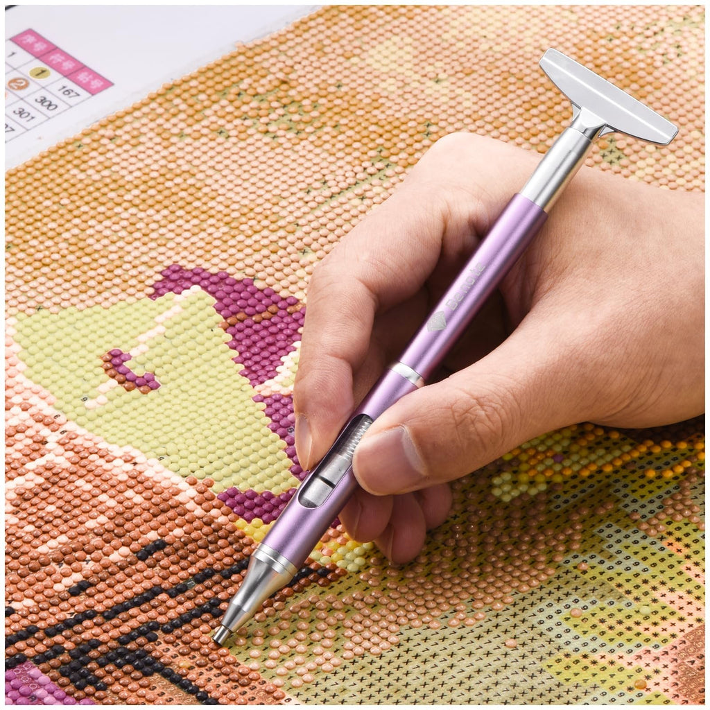 Hand holding a purple diamond art pen with a metal correction plate over a colorful diamond painting canvas.