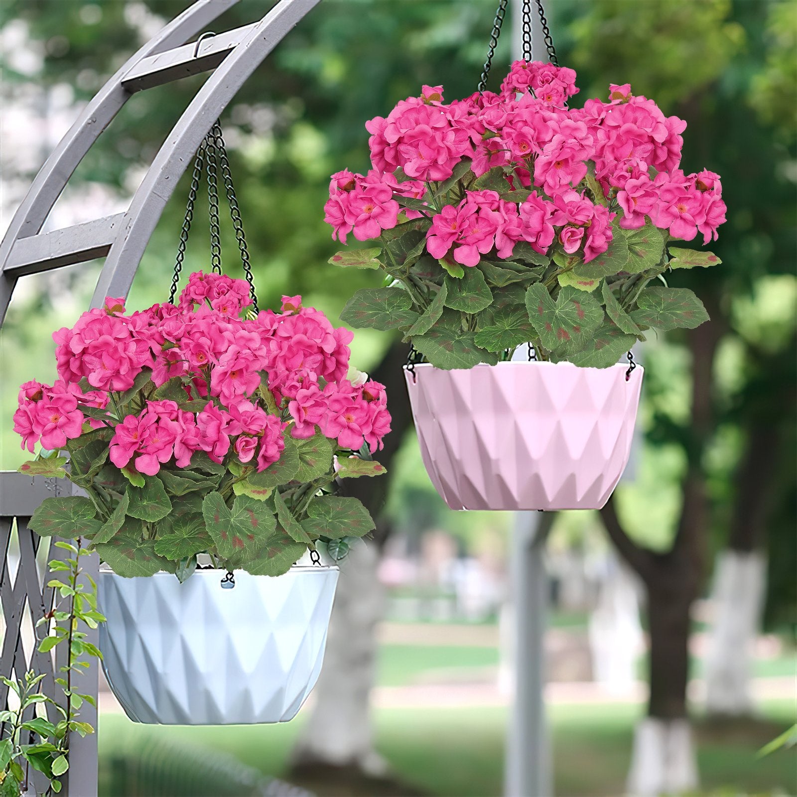 Two hanging baskets with pink artificial geranium flowers and green leaves, one in a light blue pot and one in a pink pot, displayed outdoors.