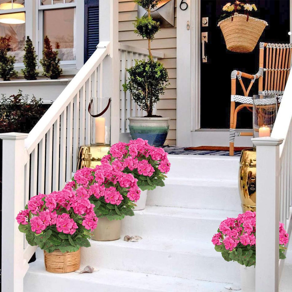 Artificial pink geranium flowers in pots on white porch steps with a chair and straw bag hanging on the door