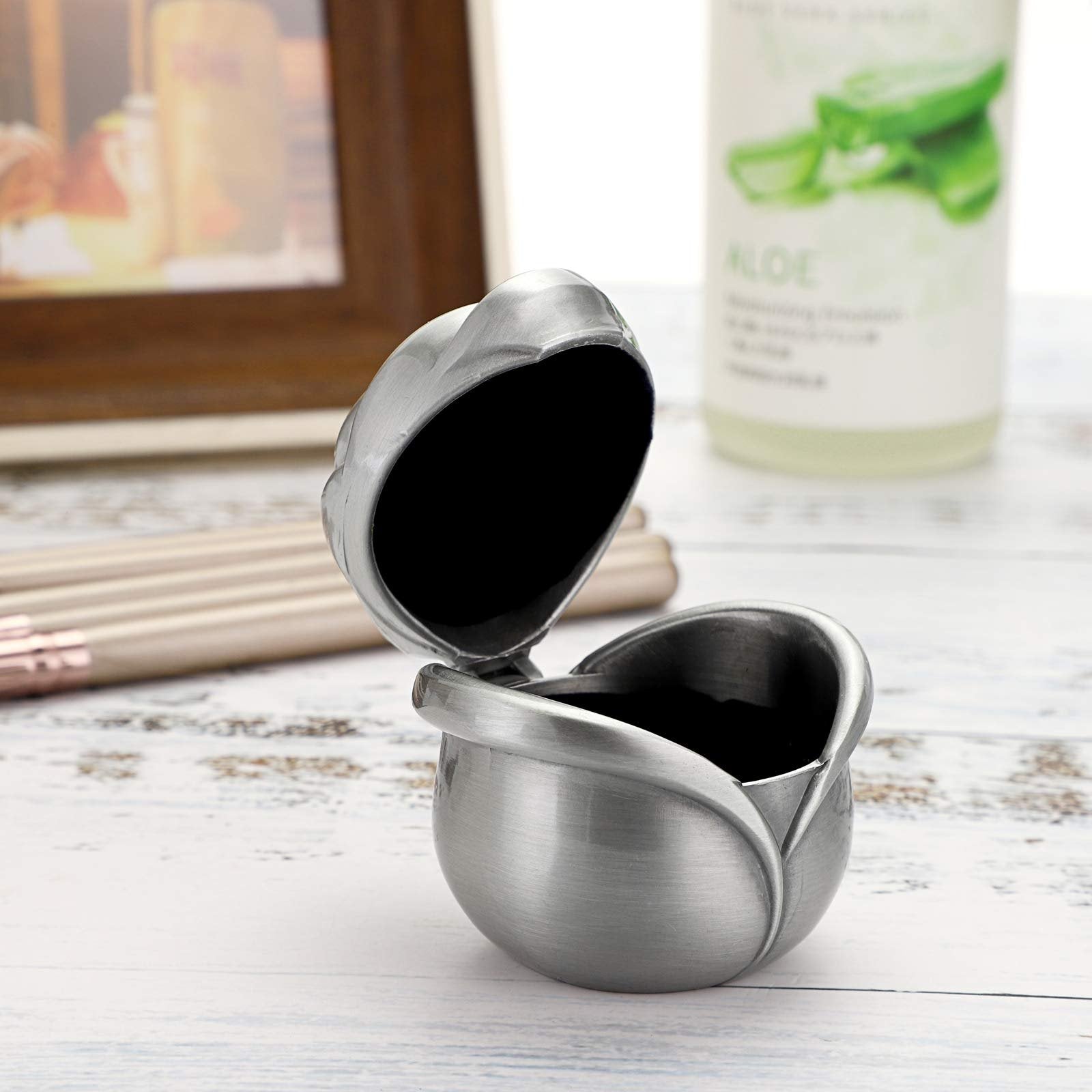 Rose-shaped vintage zinc alloy jewelry box with velvet interior, lid open, on a white wooden surface with makeup brushes and a bottle in the background.