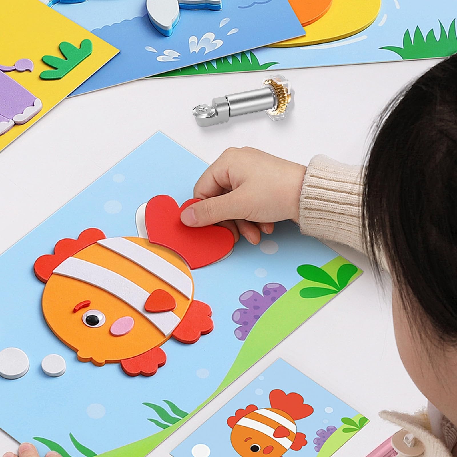 Child's hands assembling a foam fish craft with a rotary blade tool nearby.