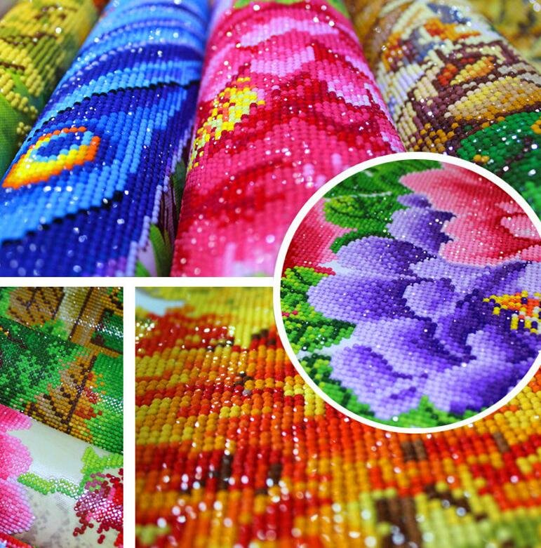 Close-up of rolled diamond painting canvases showing colorful floral and peacock feather designs, with a circular inset of a purple flower.