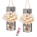 Two rustic grey distressed wood wall sconces with white flowers and LED string lights in mason jars, with a remote control.