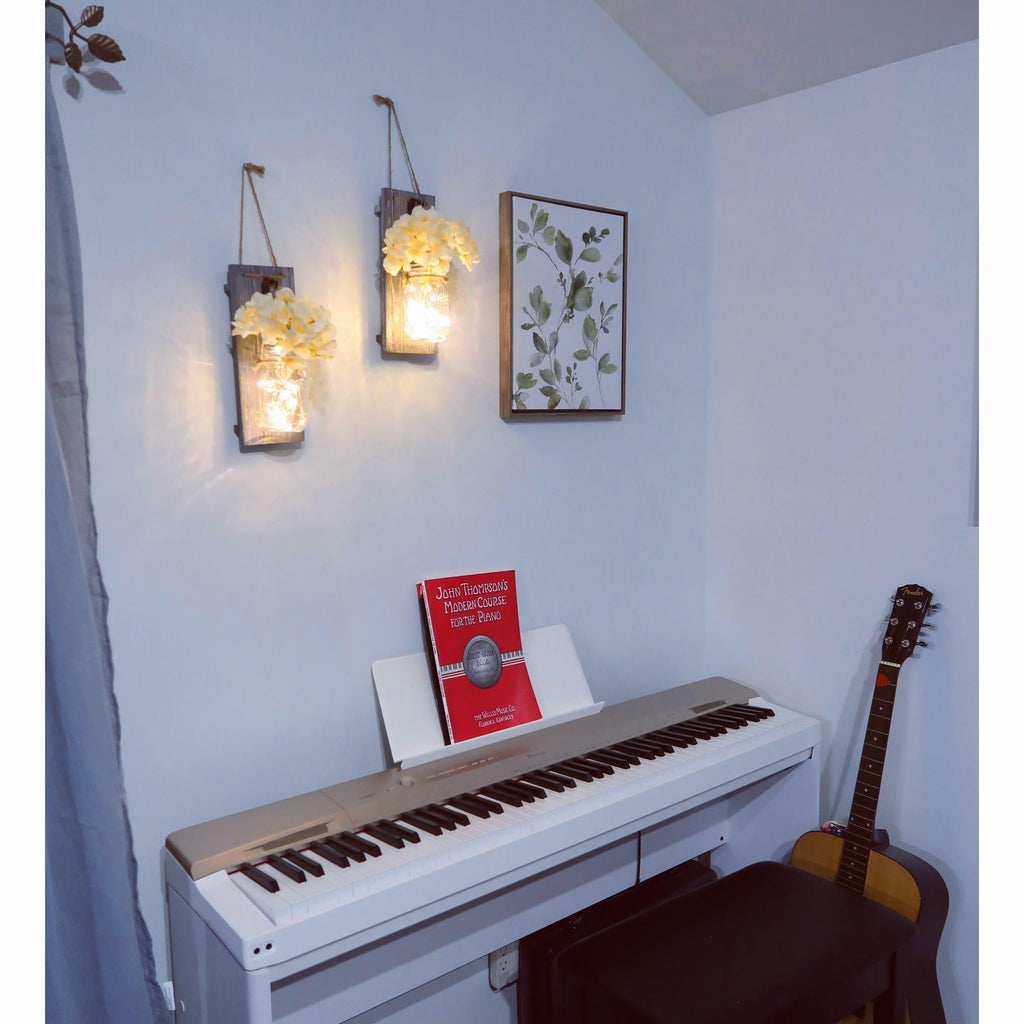 Rustic wood wall sconces with mason jars and faux flowers flanking a piano with a music book and guitar