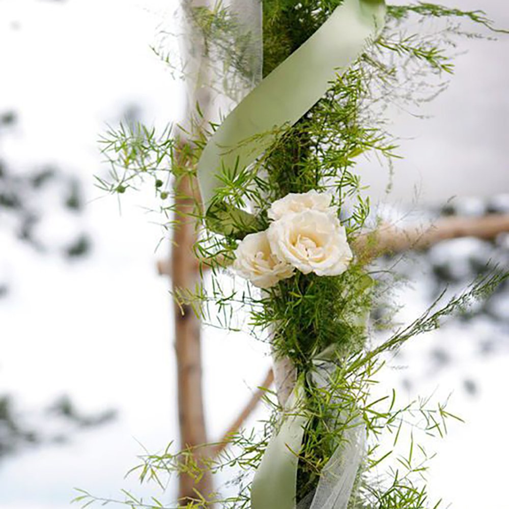 Sage green satin ribbon and white roses entwined with greenery on a decorative arch