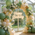 Sage green and gold balloon arch with white roses and a neon 'Happy Birthday' sign
