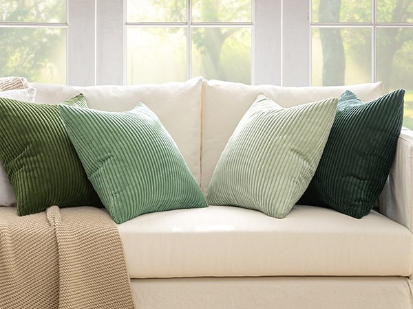 Four sage green corduroy throw pillow covers arranged on a cream-colored sofa with a knit blanket.