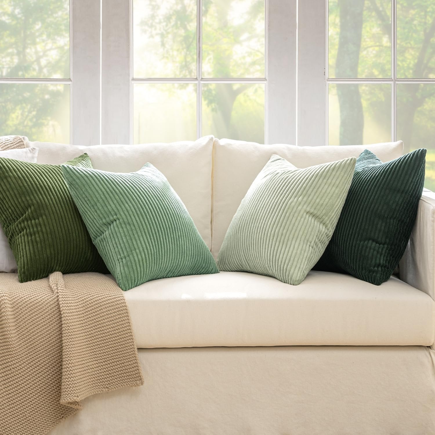 Four sage green corduroy throw pillow covers arranged on a cream sofa with a beige knit throw blanket.