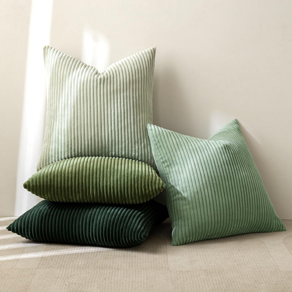 Stack of four sage green corduroy throw pillow covers in varying shades and sizes, leaning against a wall.