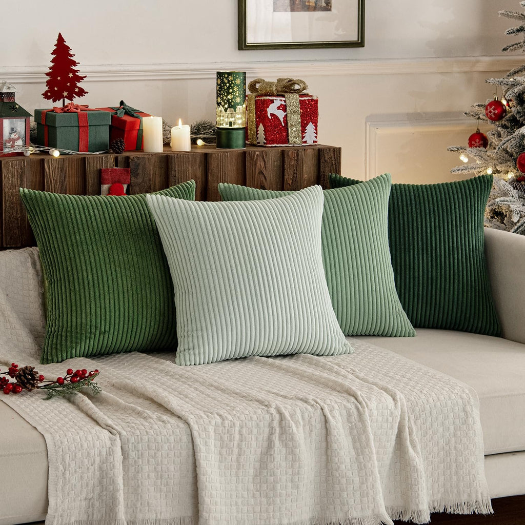 Four corduroy throw pillows in sage green and light green arranged on a couch with a cream blanket and holiday decorations.