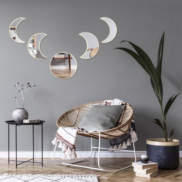 Five acrylic moon phase mirrors with beige frames arranged on a gray wall above a rattan chair.