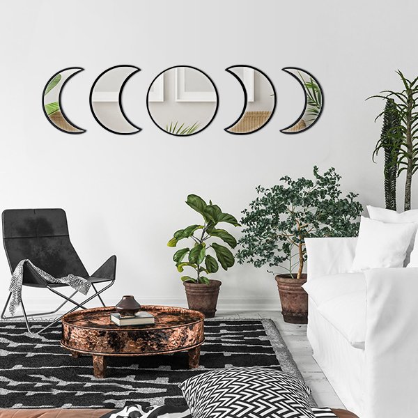 Five acrylic moon phase wall mirrors with black frames arranged on a white wall above a chair and coffee table.