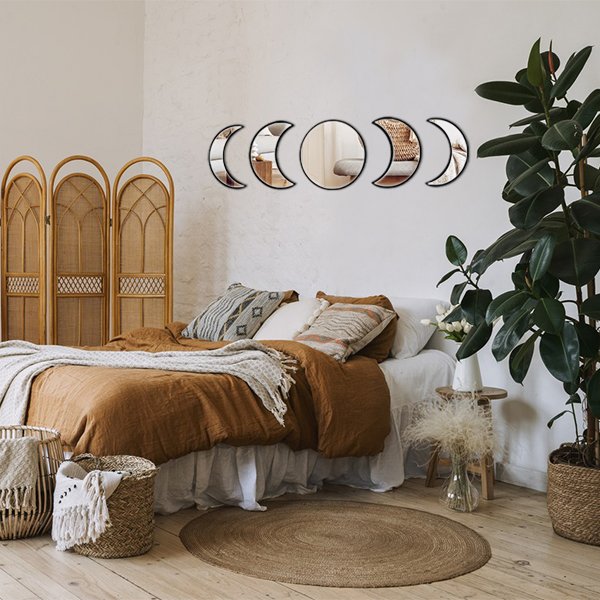 Bedroom with moon phase wall mirrors above a bed, rattan screen, and large plant.