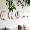 Five wooden-framed moon phase mirrors arranged on a white wall with hanging plants above and textured pillows below.
