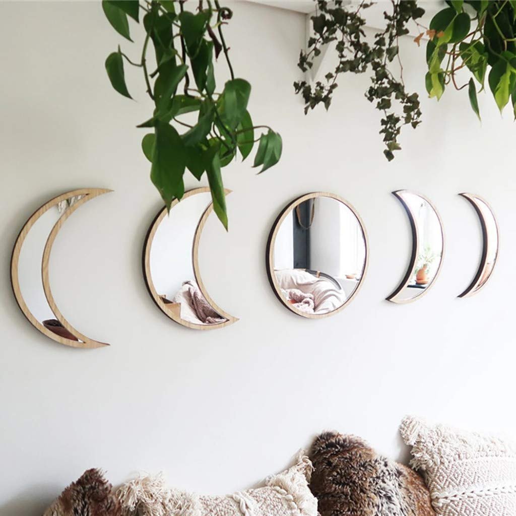 Five wooden-framed moon phase mirrors arranged on a white wall with hanging plants above and textured pillows below.