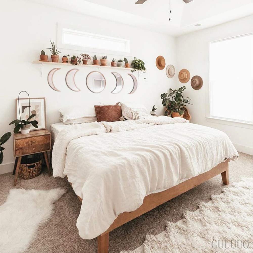 Bedroom with a white duvet on a wooden bed frame, moon phase mirrors on the wall, and potted plants.