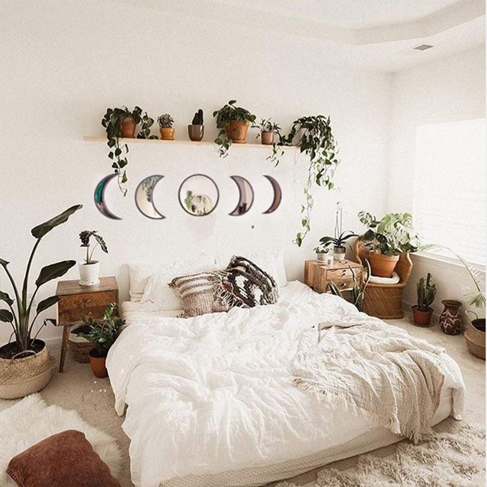 Bedroom with a bed, plants, and a set of five acrylic moon phase wall mirrors hanging above the bed.