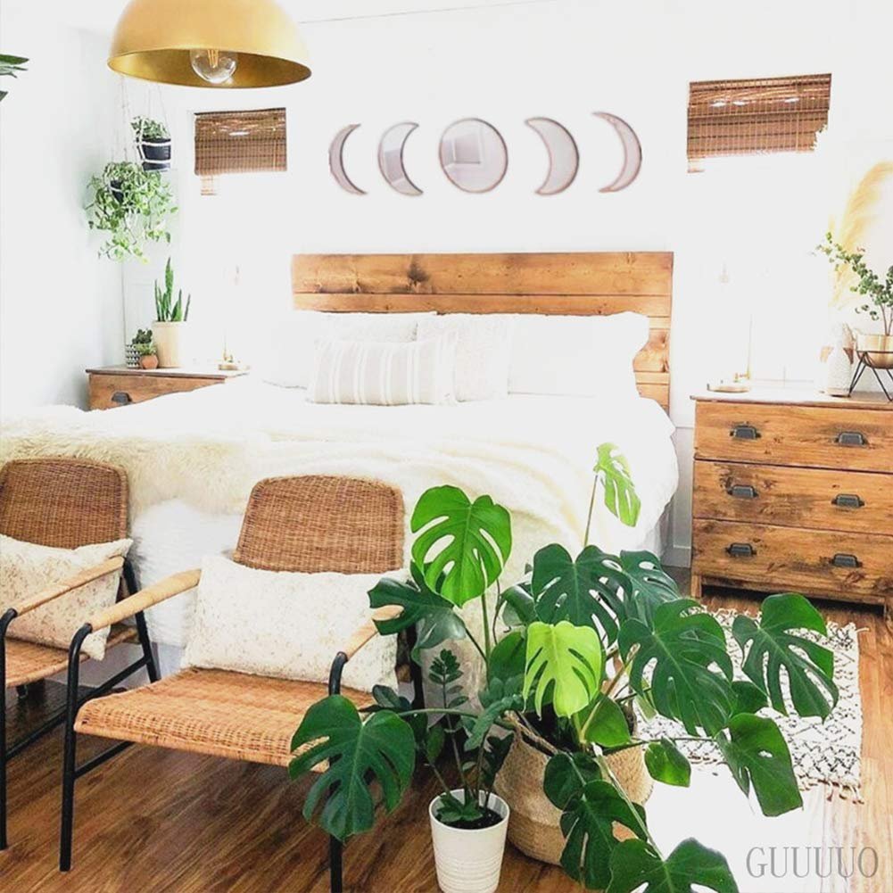 Bedroom with moon phase wall mirrors above a wooden headboard and bed, flanked by chairs and plants.