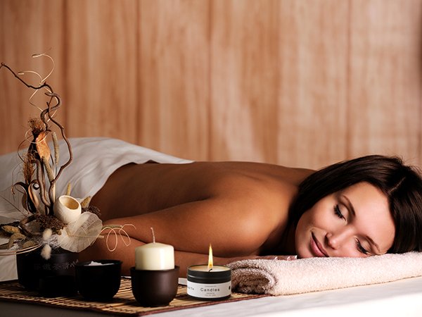 Woman relaxing on a massage table with two candles and a decorative arrangement in the foreground.